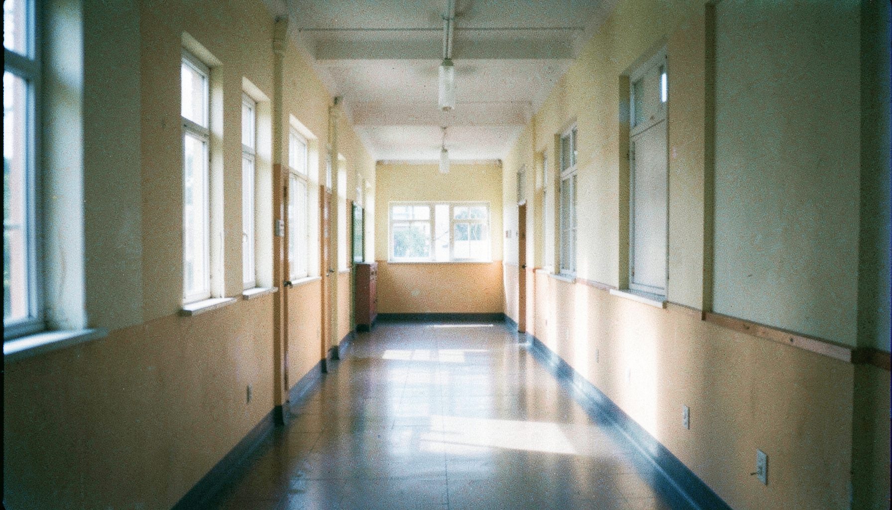 A wide sunlit hallway with soft natural light streaming through windows, warm beige and cream tones, analog film grain